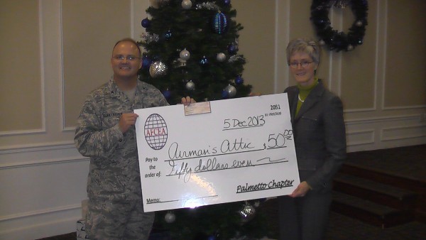 Col. Joseph Sublousky, USAF, chapter president, presents a donation to the Airmen's Attic on behalf of Sarah MacConduibh, vice president of the Air Force Portfolio, MITRE, during the chapter's December luncheon.