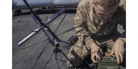 A U.S. Marine Corps Lance Corporal is assembling an AN/PRC-117G radio on the flight deck of an amphibious assault ship. The Mobile User Objective System (MUOS) adds updated firmware to the radio, giving warfighters more advanced satellite communications.” Credit: U.S. Marine Corps photo by Lance Cpl. Tawanya Norwood.