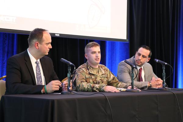 Capt. Jonathan Dodge, USA, project manager, Tactical Radios/product manager, Helicopter and Multimission Radios (c), addresses the crowd at the chapter's November luncheon, while Nick Saacks, chief, Readiness Management Division (l), and Derick Furtado, project manager, Tactical Network/product manager, Satellite Communications, look on.