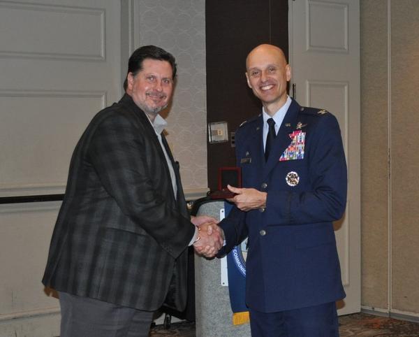 Vice President of Conferences and Symposia Tony Burris presents guest speaker, Col. Michael Cote USAF, 25th Air Force A6, with the Alamo Chapter coin during May's 