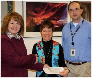 In January, Dezzutto (l) and Ranny Gaines, Booz Allen Hamilton, present a science, technology, engineering and mathematics grant to Maryann DePriest, Mirror Lake Middle School.