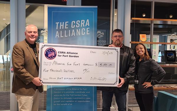 In March, Chuck Keller, presents a $5,000 check to send more than 150 students to CyberPartriot camps in 2023. Receiving the donation are Tom Clark (l) and Adanet Adon, both from the CSRA Alliance. 