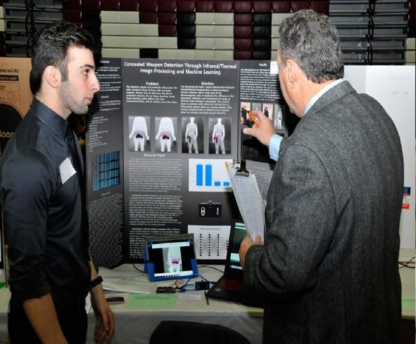 Andrew Karam (l) discusses his project, which created a neural network to detect a concealed weapon, with chapter volunteer Michael Berganski, a judge at March's Anne Arundel County Regional Science and Engineering Expo.