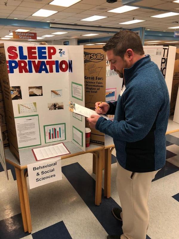 Volunteer Jeremy Martin reviews a behavioral and social sciences project on sleep deprivation at the high school's December science fair.