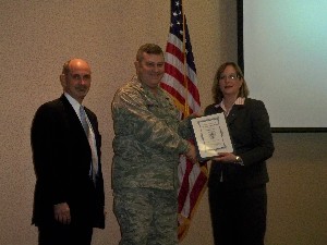 Jackie Whittaker (r), chapter president, and Dan Curtis (l), vice president for programs, shake hands with Col. Jeffrey Woolston, USAF, deputy director of communications, Headquarters Air Force Materiel Command, Wright-Patterson Air Force Base, Ohio, at the January luncheon.