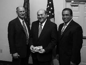 Mr. Wilson (c) is presented a Wright Brothers commemorative coin set by Chapter President Dennis Doucet (l) and Michael Bridges for speaking at the November luncheon.
