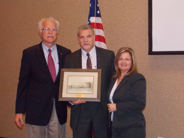 Outgoing board member Craig McComb (c), deputy chief information officer of the Air Force Life Cycle Management Center, receives a print from Rick Wegmann, board president, and Skinner at the July luncheon.