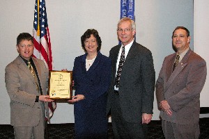Presenting a plaque of recognition are Tritle (far l) and Norman Nelson, chapter corporate membership director (far r), who honored JELCO Incorporated as a new corporate member.