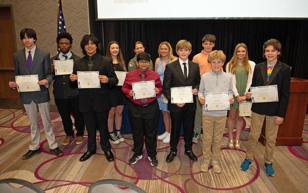 Anthony stands surrounded by 11 of the award recipients from the Omaha Metropolitan Science and Engineering Fair who were featured at the April luncheon.  Students pictured (l-r) are:  Thanakorn Newman, Omaha Central High School, Omaha, Nebraska, 11th grade, Freshwater Instrument for Sampling the Hydrosphere; Matthew Lewis, Omaha Central High School, 11th grade, Freshwater Instrument for Sampling the Hydrosphere; Christopher Mendoza, Omaha North High School, 12th grade, Continuous Data Assimilation on the MHD Equation; Kaelynn Edwards, Lifegate Christian School, Omaha, Nebraska, 8th grade, Hail No!; Vidyuth Sarathy, Elkhorn Valley View Middle School, Elkhorn, Nebraska, 6th grade, From Router to Room: Tracking Wi-Fi Signal and Speed Across Homes; Kinlee Huber, Buffett Middle School, Omaha, Nebraska, 7th grade, Can a 3D Printed Bolt Replace a Real Bolt; Oliver Fondren, Odyssey Academy, Omaha, Nebraska, 7th grade, Fins for Flight; Billy McColgan, St. Margaret Mary School, Omaha, Nebraska, 7th grade, Squeak Performance; Louie Smith, St. Margaret Mary School, Omaha, Nebraska, 7th grade, Squeak Performance; Stella Lucille Moon, Buffett Middle School, 8th grade, Watts Up?; and Jackson Stockdale, Buffett Middle School, 8th grade, Ultrasonic Levitation. All projects were assessed at the Henry Doorly Zoo in March. The chapter awarded a total of $1,800.