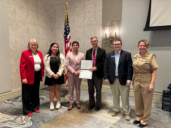 (l-r) Teresa Duvall, outgoing education chair; Andrea Aguas, student, Catholic High School, Norfolk, Virginia; Sebastian Rodriguez, student, Catholic High School; Adam Lewandowski, teacher, Catholic High School; Matthew Umphlet, STEM Teaching Tool Awards chair; and Capt. Christina Hicks, chief of staff of U.S. Fleet Cyber Command, commander, TENTH Fleet, pose for a photo at the January event.

