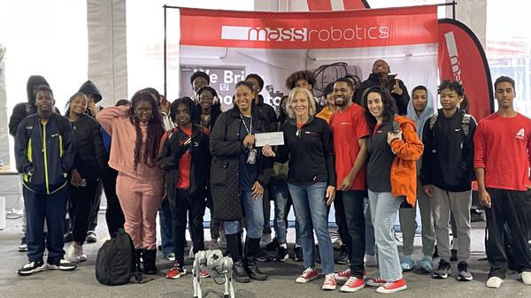 Joyce Sidopoulos, chapter board member and co-founder and chief of operations at MassRobotics (front center r), and MassRobotics STEM educators Alethea Campbell and Kevin Smith (front row, far r), present STEM educator Stephanie Pottinger-ONeal, New Mission High School Computer Essentials Teacher (front center l), and students, a check for $2,000 in October.