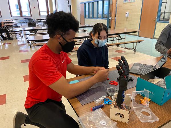 Khalif Mitchell, volunteer, The MITRE Corporation, assists student with building a robotic hand during the chapter and MassRobotics collaboration to promote STEM education in April. 