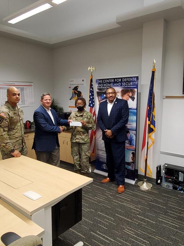 Previously postponed, the chapter's award ceremony takes place in August at Fayetteville State University. Cadet Desiree Bliss (c) receives an award from Marv Gordner, chapter president. Maj. Louis Hare, Army ROTC, assistant professor of military science, and John Bellamy, executive director, Defense and Homeland Security, join in the photo.