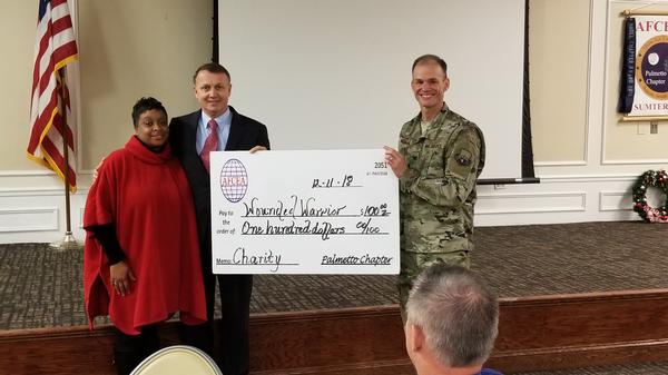 Collette Jones and Col. Keith Mueller, USAF, Air Forces Central Command, A-6, director of communications and information, present a $100 donation to the Wounded Warroir Project on behalf of Gen. Matthews at the December luncheon.