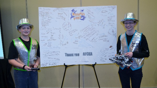 In February, Jake (l) and Jenna Gulick, team leads for the FIRST Lego League (FLL) team Da Ex Bots, display their FLL trophy and winning Lego robot flanking a thank you card to AFCEA from the teams that competed in the rescheduled Southern IL FLL tournament.