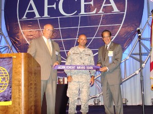 At the LandWarNet Conference in August, Kent Schneider (l), president and chief executive officer of AFCEA International, and Paul Cofoni (r), chair of AFCEA's board, present Col. Mark Churchwell, USA, director, command, control, communications, computer systems and information, Headquarters U.S. Southern Command, and chapter president, with the chapter's achievement award.
