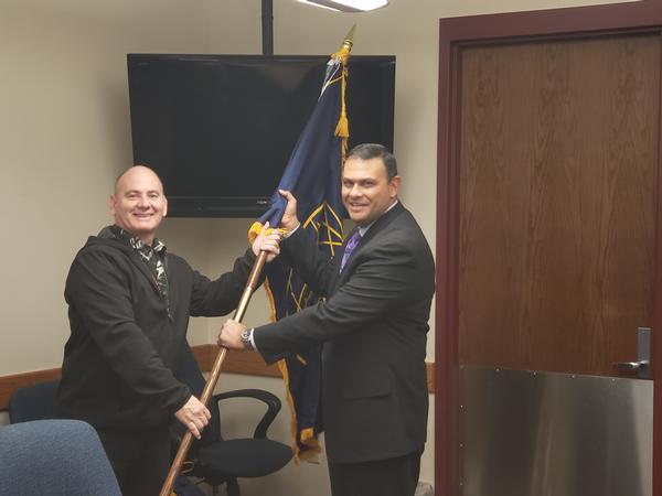 Larry Woehl, departing chapter president (l), passes the flag to Gonzalez, incoming president, at the December meeting.