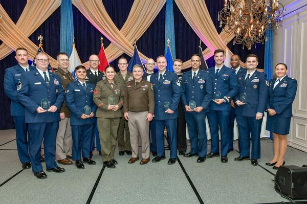 In May, 18 exceptional men and women are recognized. Pictured are (l-r) IT1 Michael Reeve, USCG; Master Sgt. Joseph Metelko, USAF; Maj. Matthew Sinda, USA; Senior Airman Jonathan Rush, USAF; SFC Charles Studer, USA; Sgt. Samantha Delgado, USMC; Maj. Michael Lehmer, USMC; Lt. Gen. William J. Hartman, USA, U.S. Cyber Command; Master Sgt. Benjamin Zufelt, USAF; Tech Sgt. Joseph Allen, USSF; IT1 Nichola Isaak, USN; Maj. Roberto Molineros, USSF; Lt. j.g. Justin Steiner, USCG; Capt. LaVell Williams, USAF; Tech Sgt. Franko Salajcik, USAF; and Maj. Michelle Smith, USAF.