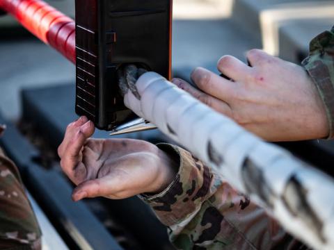 A Civil Engineer Squadron electrical power production journeyman inserts a metal wire into an encasing for a ground automobile retractable barrier net, at Dover Air Force Base, Delaware. Credit: Senior Airman Marco A. Gomez, U.S. Air Force