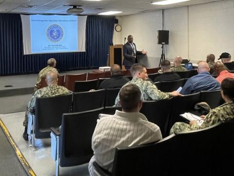 In 2022, Cecil McGee, Electromagnetic Spectrum Operations Training Team fleet liaison, briefs on electromagnetic spectrum operations (EMSO) at the first Strike Force Interoperability Officer symposium hosted by Naval Information Forces. Robust EMSO is needed against future threats. Credit: U.S. Navy photo by Naval Information Forces
