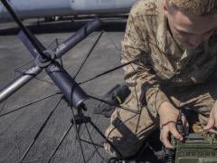 A U.S. Marine Corps Lance Corporal is assembling an AN/PRC-117G radio on the flight deck of an amphibious assault ship. The Mobile User Objective System (MUOS) adds updated firmware to the radio, giving warfighters more advanced satellite communications.” Credit: U.S. Marine Corps photo by Lance Cpl. Tawanya Norwood.
