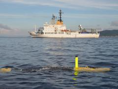 The MUSCLE autonomous vehicle developed by the Centre for Maritime Research and Experimentation, or CMRE, for mine countermeasures works with the NATO Research Vessel Alliance (in the background). The autonomous vehicle is equipped with synthetic aperture sonar.