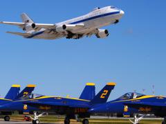 A Boeing E-4B, an airborne command post, flies over the U.S. Navy Blue Angels F-18s during an air show. The E-4B serves as the National Airborne Operations Center for the president and secretary of defense. In case of national emergency or destruction of ground command control centers, the E-4B provides a survivable, command, control and communications center to direct U.S. forces, execute emergency war orders and coordinate actions by civil authorities.