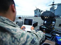 Senior Amn. Xavier Rubio, USAF, tests a satellite communications dish aboard the amphibious dock landing ship USS Pearl Harbor.
