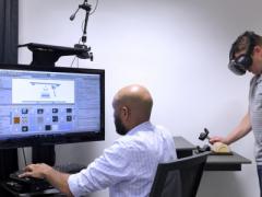 Andrew Sweeney, seated, and another industrial designer with Battelle’s Human Centric Design group use virtual reality technology to get user feedback about a hand-held medical device.