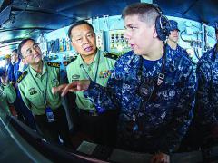 Seaman Alex Snyder, USN, right, explains the functions of the helm on the navigation bridge of the aircraft carrier USS George Washington to Maj. Gen. Chen Weizhan, deputy commander of the People’s Liberation Army, Hong Kong Garrison, center, and Col. Li Jiandang, Hong Kong Garrison liaison officer during a distinguished visitor embark.
