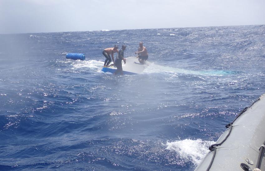 Suspected drug smugglers stand on top of a sinking vessel approximately 90 miles south of Haiti. The USS St. Louis launched a small boat to rescue the suspected smugglers after their vessel capsized. Credit: U.S. Coast Guard