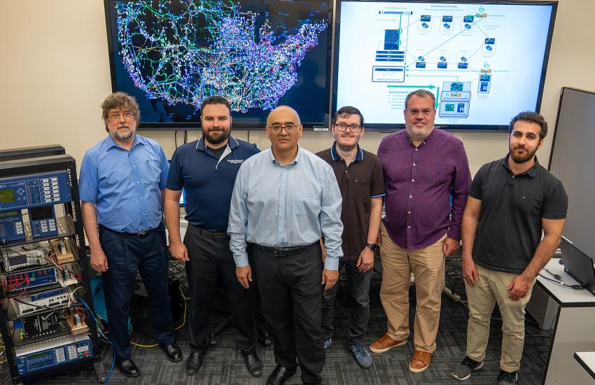 Members of the GridLogic research team pose with a display showing (l) a visualization of the power grids, water systems and oil/gas pipelines in the United States and (r) a proposal for network security monitoring in a power grid. Shown are (l-r) David Huggins, Trevor Lewis, Santiago Grijalva, Fabricio Ceschin, Vincent Mooney and Arman Allahverdi. Credit: Marion Crowder, Georgia Tech