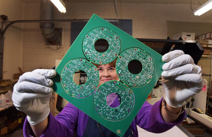 Judy Ortiz Rizek, owner and president of The Circuit Shop in Albuquerque, New Mexico, shows an example of printed circuit boards manufactured for Sandia National Laboratories. Sandia, in turn, houses a microelectronics counterfeit detection center that “rigorously assesses commercially produced microelectronics to verify that they are free of vulnerabilities.” Credit: Sandia photo by Randy Montoya