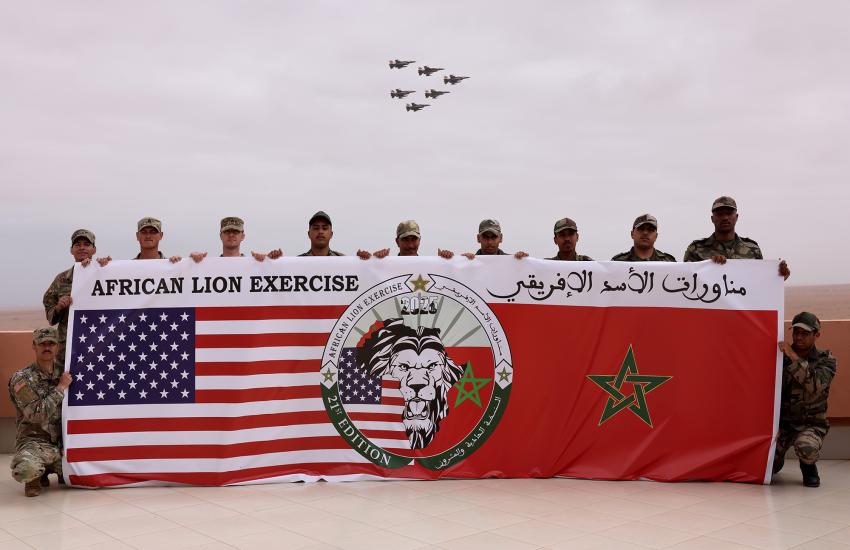 U.S. Marines and Soldiers from the Royal Moroccan Armed Forces pose for a group photo while F16 fighter jets pass overhead at Cap Draa during AL25 in TanTan, Morocco, May 2025. 