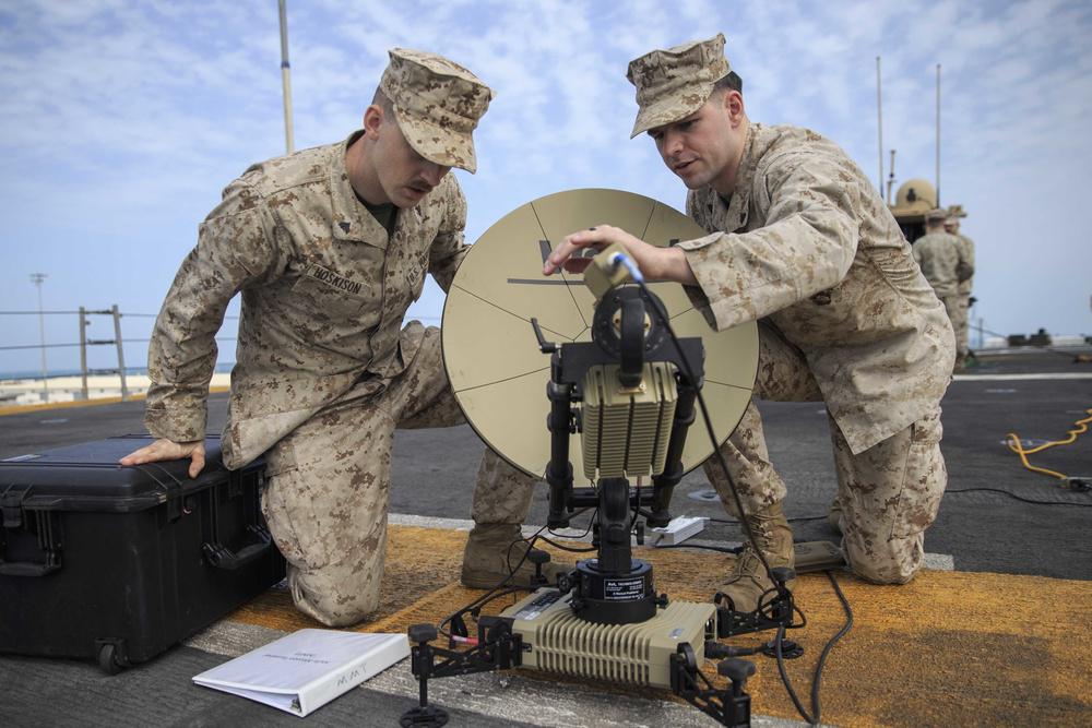 U.S. Marine Corporals Josrdan Hoskison (l) and Jacob Jusczak, both data system administrators with the 22nd Marine Expeditionary Unit, set up a Multi-Mission Terminal satellite on the flight deck of the Wasp-class amphibious assault ship USS Kearsarge (LHD-3). The satellite enables secure access to Internet Protocol broadband networks and the establishment of command post communications from any location. Credit: Tawanya Norwood, 22nd Marine Expeditionary Unit