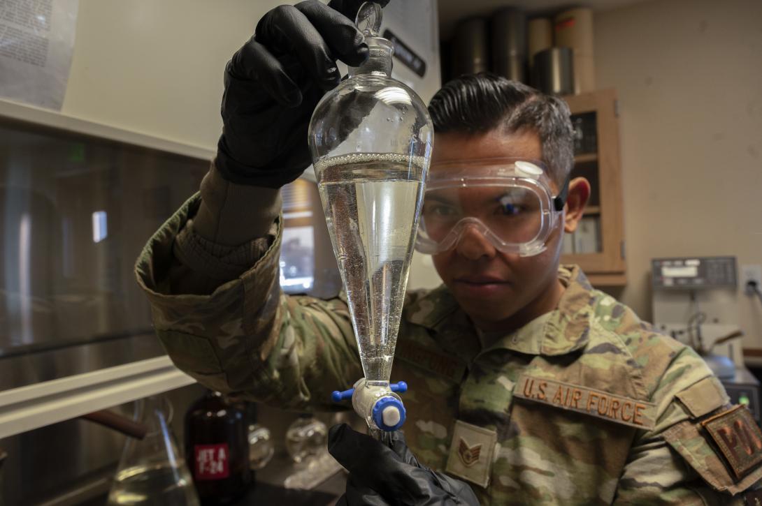 A U.S. Air Force staff sergeant inspects a flask of jet fuel as part of quality control measures. Reducing fuel consumption is a major element of Air Force climate change efforts. Credit: U.S. Air Force