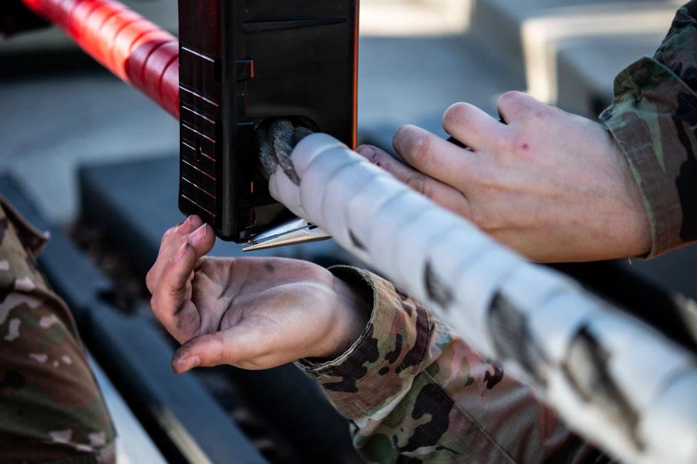 A Civil Engineer Squadron electrical power production journeyman inserts a metal wire into an encasing for a ground automobile retractable barrier net, at Dover Air Force Base, Delaware. Credit: Senior Airman Marco A. Gomez, U.S. Air Force