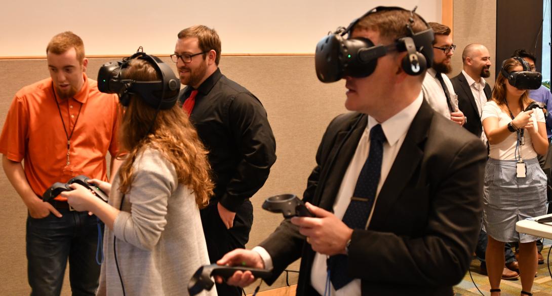 Two engineers fly around the topside of Navy ships via virtual reality while a third explores the interior of an amphibious transport dock ship’s pilot house. Photo credit: U.S. Navy.