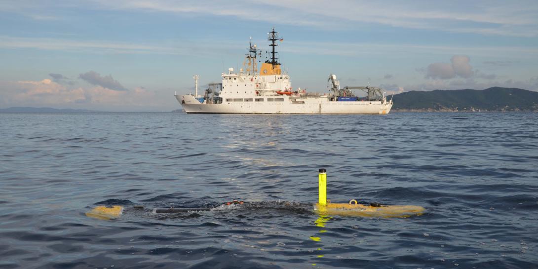 The MUSCLE autonomous vehicle developed by the Centre for Maritime Research and Experimentation, or CMRE, for mine countermeasures works with the NATO Research Vessel Alliance (in the background). The autonomous vehicle is equipped with synthetic aperture sonar.