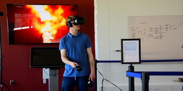 Jack Lewis, a NIST associate, demonstrates the use of a virtual reality headset and controllers with NIST’s virtual office environment in which first responders search for a body in a fire. Credit: Burrus/NIST