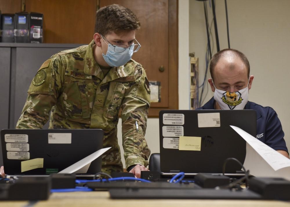 Airman 1st Class Tristan Williams, USAF, 4th Communications Squadron, communications focal point client systems technician (left), and Timothy Leineke, computer support technician for the squadron, examine ways to remotely add computers to the network at Seymour Johnson Air Force Base, North Carolina, in September 2020. DISA is developing robotic process automation solutions to aid such security authorization processes, saving time and workloads.  U.S. Air Force photo by Airman 1st Class Kimberly Barrera