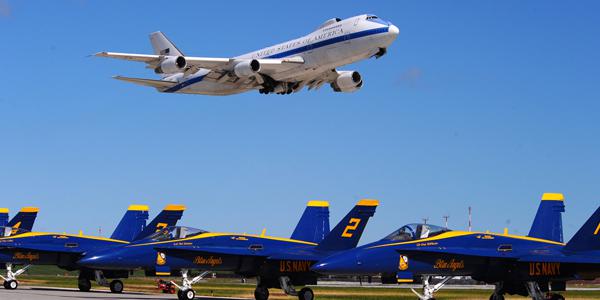 A Boeing E-4B, an airborne command post, flies over the U.S. Navy Blue Angels F-18s during an air show. The E-4B serves as the National Airborne Operations Center for the president and secretary of defense. In case of national emergency or destruction of ground command control centers, the E-4B provides a survivable, command, control and communications center to direct U.S. forces, execute emergency war orders and coordinate actions by civil authorities.