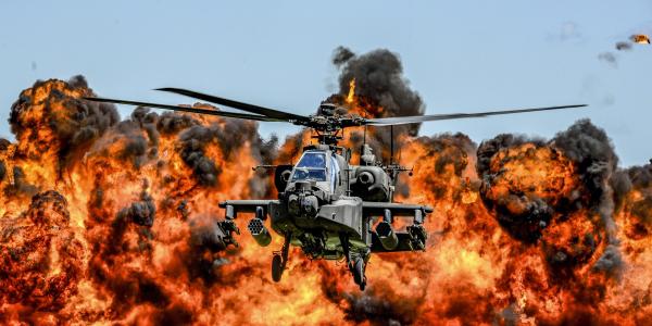An AH-64D Apache attack helicopter flies in front of a wall of fire during the South Carolina National Guard Air and Ground Expo at McEntire Joint National Guard Base, South Carolina, in 2017. Air National Guard photo by Tech. Sgt. Jorge Intriago