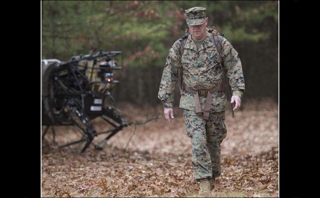 Brig. General Kevin Killea, USMC, Marine Corps Warfighting Laboratory commanding general, leads the Legged Squad Support System through the woods at Fort Devens, Mass. Wearing a special pack fitted with thick black bands that the robot is programmed to identify and track, the general led LS3 through the woods over uneven and sometimes tricky terrain.