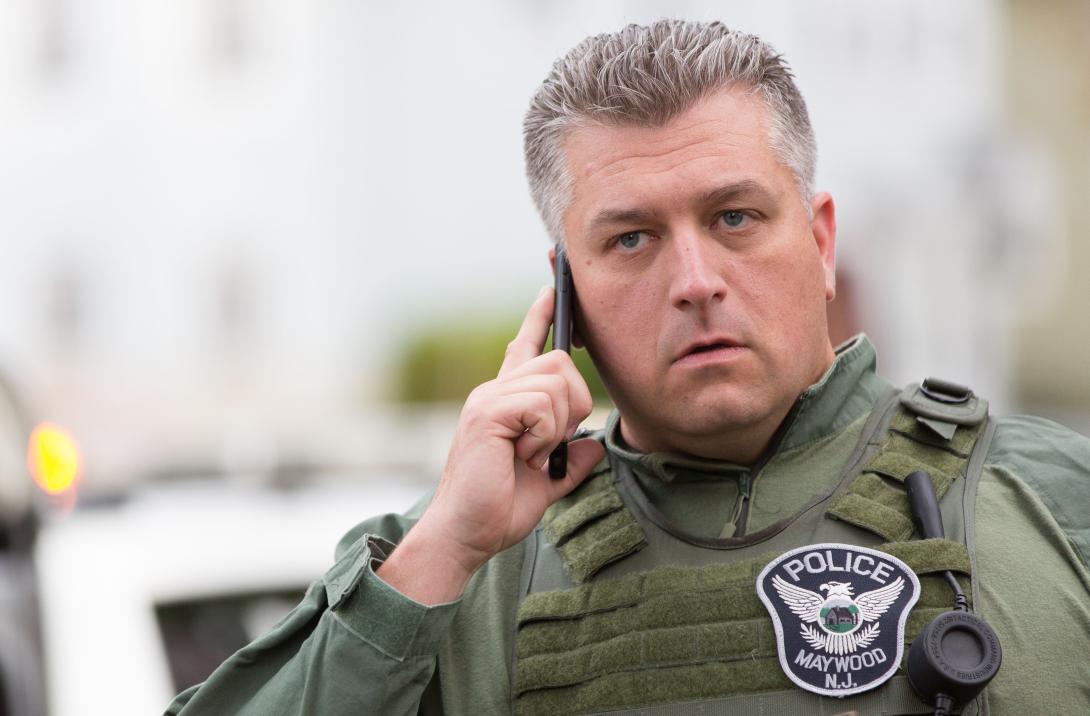 A police officer uses a smartphone at a crisis scene. The introduction of broadband devices is creating interoperability problems for emergency responders used to conventional radio communications.