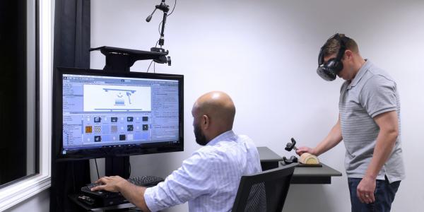 Andrew Sweeney, seated, and another industrial designer with Battelle’s Human Centric Design group use virtual reality technology to get user feedback about a hand-held medical device.