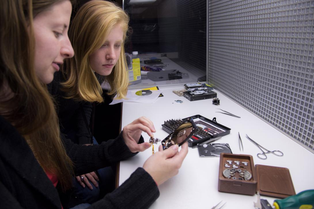 SPAWAR SSC Atlantic intern Sage Glidewell looks on as employee Alisha Slebodnik examines the internal components of a computer hard drive. SSC Atlantic develops, acquires and provides life cycle support for C4ISR systems, information technology and space capabilities. The new Information Warfare Research Project aims to boost the Navy’s C4ISR capabilities. Credit: U.S. Navy photo by Joe Bullinger