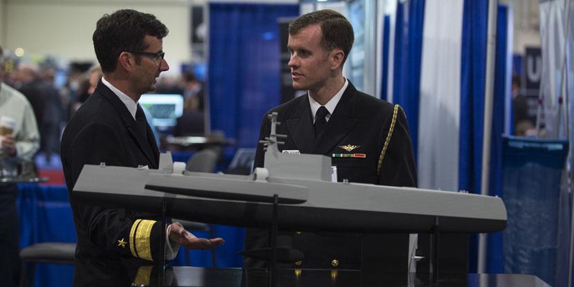 Rear Adm. Christian "Boris” Becker, USN, commander, SPAWAR (l), discusses naval capabilities with another officer while visiting the Office of Naval Research and Naval Research Laboratory  exhibit at the Navy League’s Sea-Air-Space Exposition last year. SPAWAR System Command’s recent Other Transaction Agreement (OTA) award for its Information Warfare Research Project  will drive key innovative information warfare capabilities to the Navy, Rear Adm. Becker says. Credit: U.S. Navy photo by John F. Williams