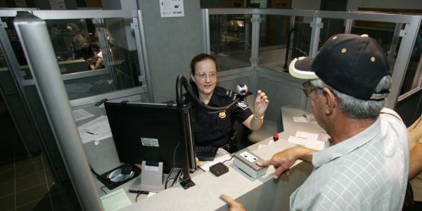 A Customs and Border Protection officer takes biometrics from an arriving foreign visitor. Integrating biometrics into the pre-arrival vetting process is one of the National Vetting Center’s key tasks.  Customs and Border Protection