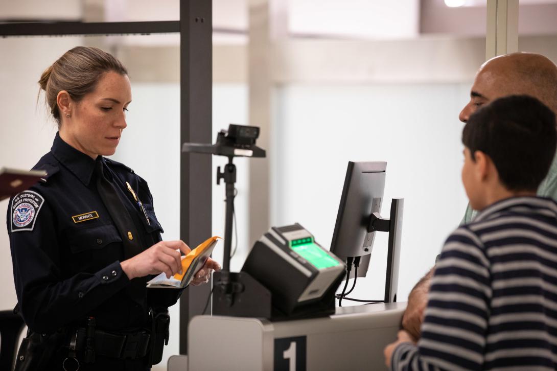 A Customs and Border Protection officer examines travel documents of arriving foreign visitors. All visitors applying for entry to the United States under the Visa Waiver Program are vetted through the National Vetting Center.  Customs and Border Protection